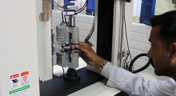 Engineer conducting a material strength test using a tension compression tester in a lab